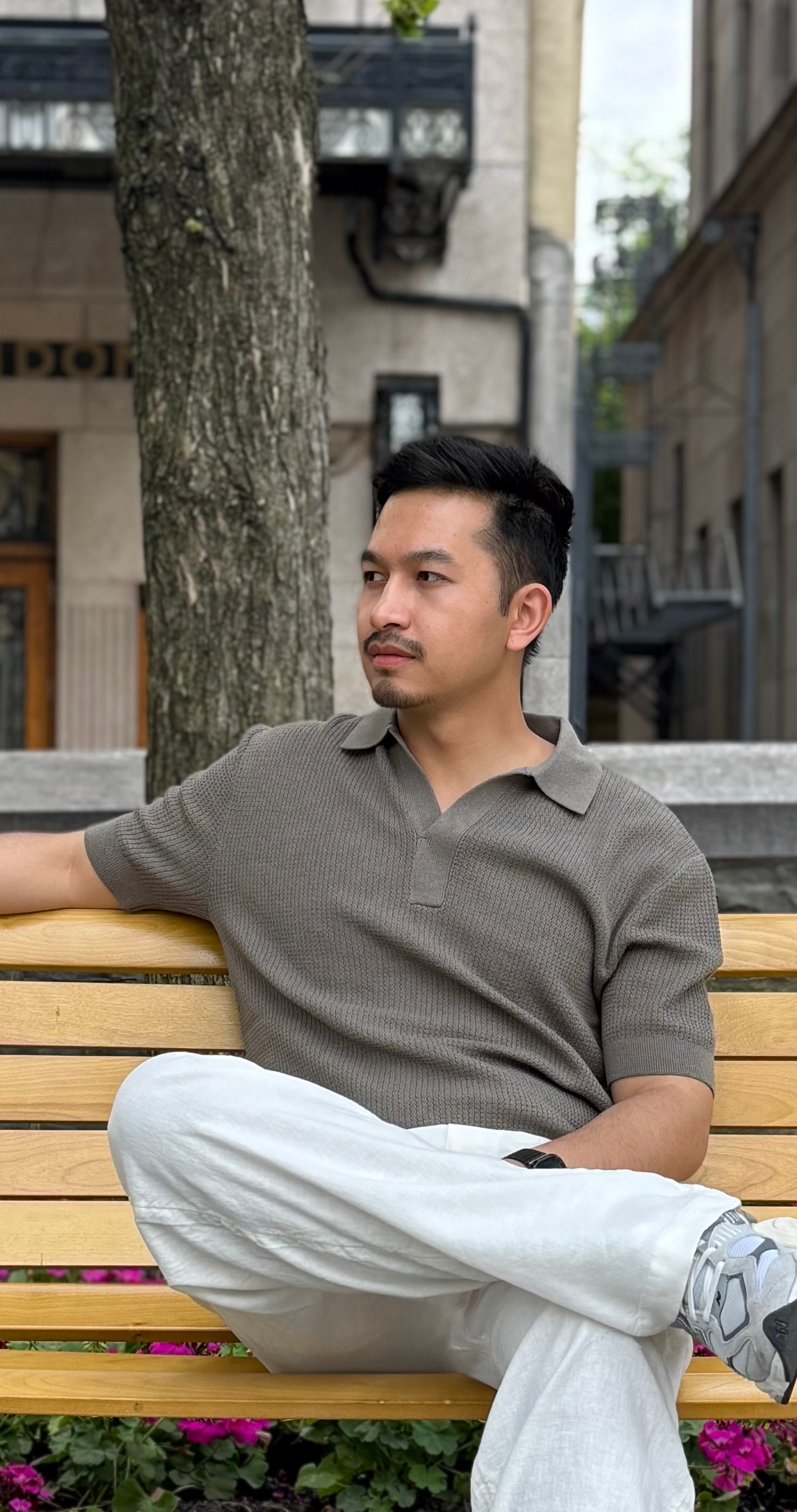 Man in an olive knit polo sitting on a park bench in front of Hotel Clarendon, Quebec City